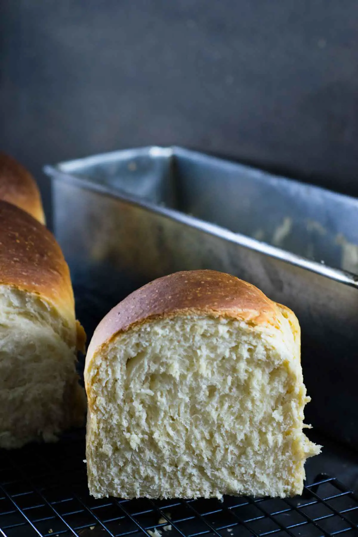 Imagem de pão caseiro, mostrando o pão cortado ao meio, em primeiro plano e a forma ao fundo
